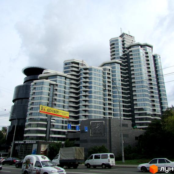 Житловий комплекс PecherSKY з багатоповерховими будівлями, скляними фасадами та балконами. На передньому плані дорога з автомобілями та зелені насадження.