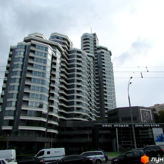 Багатоповерховий Житловий комплекс PecherSKY з темно-сірим фасадом та світлими балконами. На першому поверсі розташований офіс продажу, поруч проїжджа частина з автомобілями.