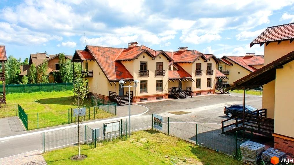 Зображення житлового будинку в Котеджному містечку Садок Вишневий. Будинок з червоним дахом та світлими стінами, облаштована прибудинкова територія з газоном та парканом.