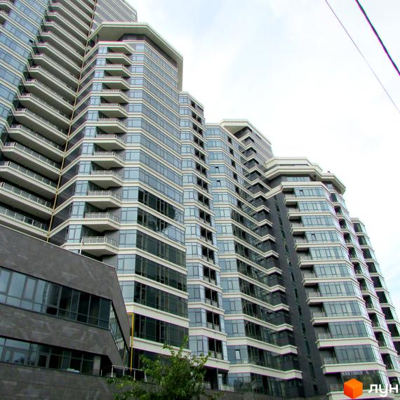 Багатосекційний житловий комплекс PecherSKY з скляними фасадами, балконами та сірими стінами, оточений зеленню.