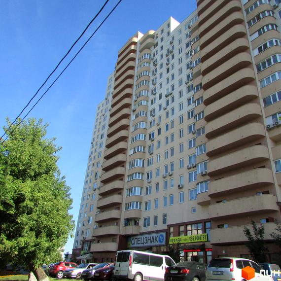 Житловий комплекс Ново-Деміївський з фасадом та балконами, прибудинкова територія з автомобілями та зеленими насадженнями.