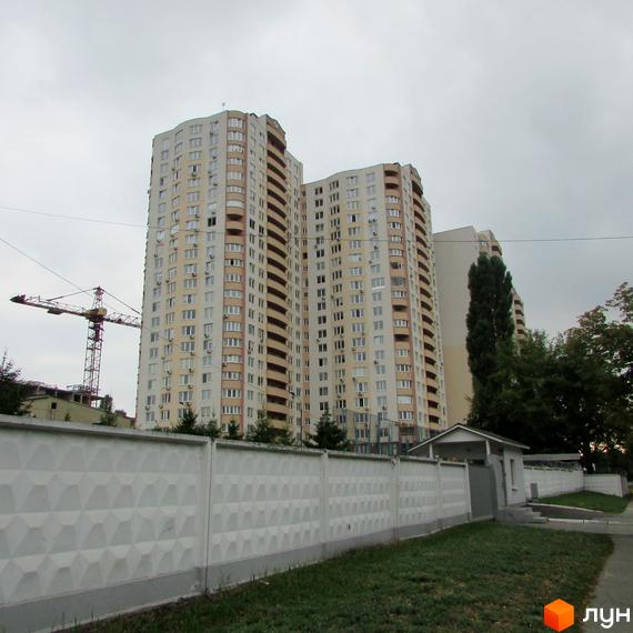 Житловий комплекс Ново-Деміївський, висотний будинок з великою кількістю вікон та прибудинковою територією з зеленими насадженнями.