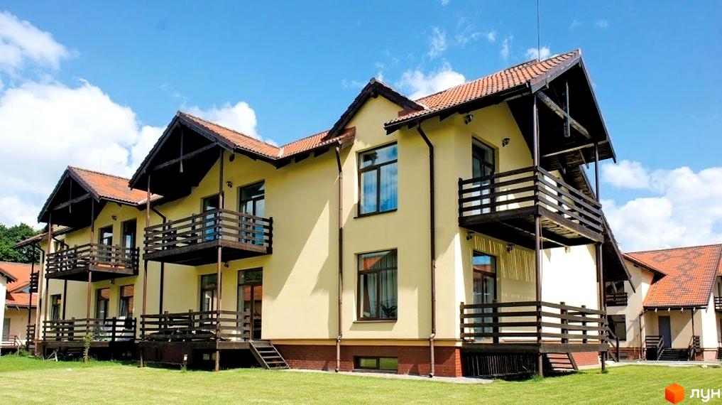 Зображення будинку в Котеджному містечку Садок Вишневий. На фото видно двоповерховий будинок з балконами та терасами, розташований на зеленій прибудинковій території.