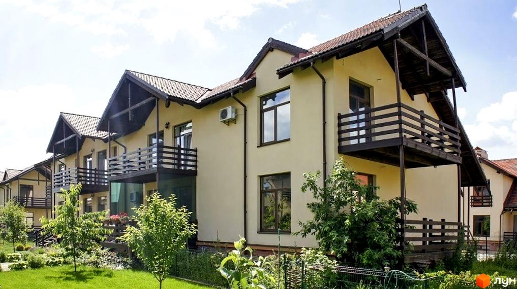 Зображення житлового комплексу з двоповерховими будинками з балконами. На території є зелені насадження та газон.