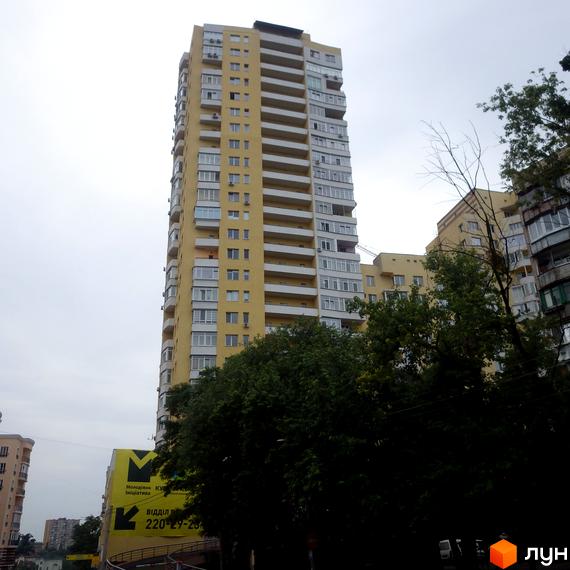 Вид на житловий комплекс ЖК Затишний з жовтою фасадною частиною та балконами. Прибудинкова територія з зеленими насадженнями.