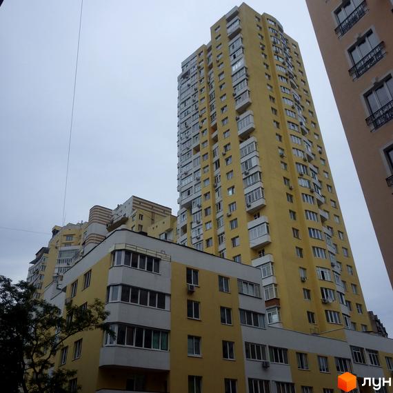 Вид на житловий комплекс Затишний з жовтою фасадною обробкою та великими вікнами. Прибудинкова територія з зеленими насадженнями.