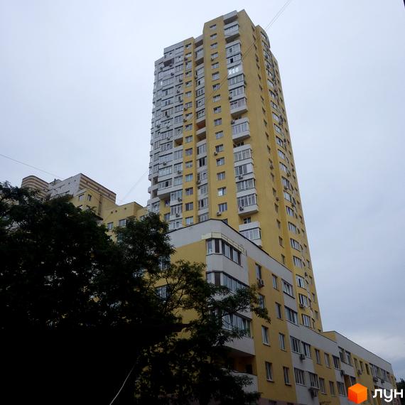 Житловий комплекс Затишний з жовтою фасадною обробкою та великими вікнами. Прибудинкова територія озеленена деревами та кущами.