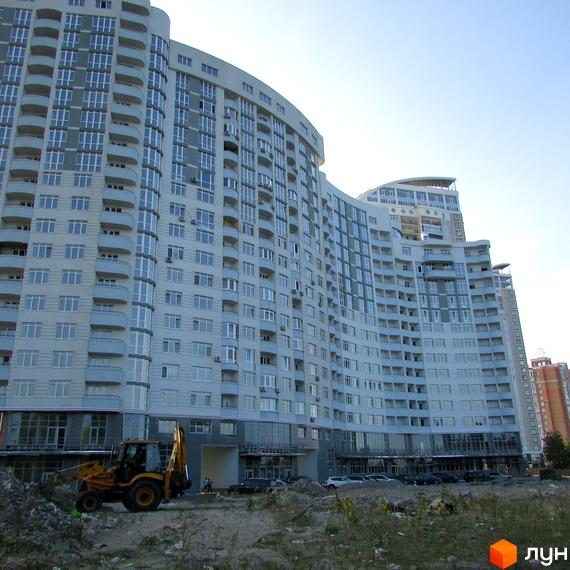 Житловий комплекс Парк Стоун - велика новобудова з вигнутим фасадом та численними балконами. Перед будинком видно будівельну техніку та ділянку з травою.