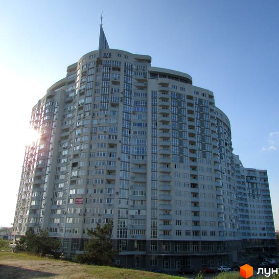 Житловий комплекс Парк Стоун - висотна будівля з багатою поверховістю та балконами, на тлі блакитного неба. Навколо будівлі зелена зона та припарковані автомобілі.