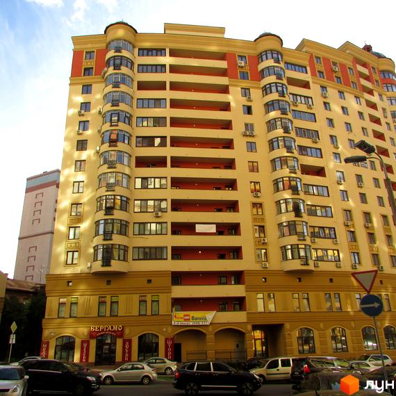 Зовнішній вигляд багатоповерхового житлового комплексу ЖК Златоустівський з жовто-червоним фасадом та балконами. На першому поверсі розташовані магазини.