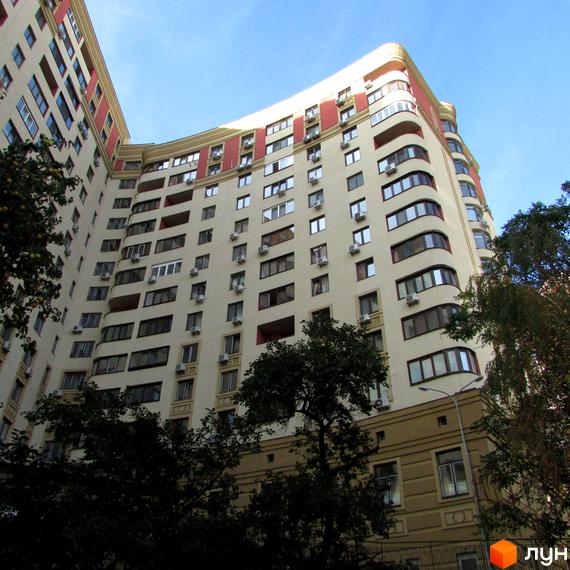 Житловий комплекс Златоустівський – багатоповерхова будівля з вигнутим фасадом, оздоблена червоними елементами та численними кондиціонерами. Навколо будинку ростуть дерева.