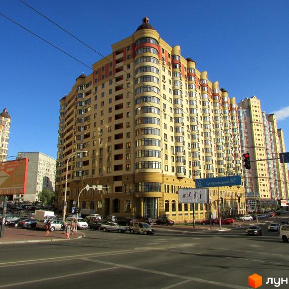 Житловий комплекс Златоустівський - висотна новобудова з багатоповерховими секціями та вигнутими фасадами. Перед будинком проїжджа частина та припарковані автомобілі.