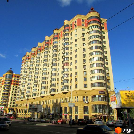 Житловий комплекс Златоустівський - висотна новобудова кремового кольору з червоними елементами фасаду, багатоповерховий будинок з численними балконами та вікнами, розташований на фоні блакитного неба.