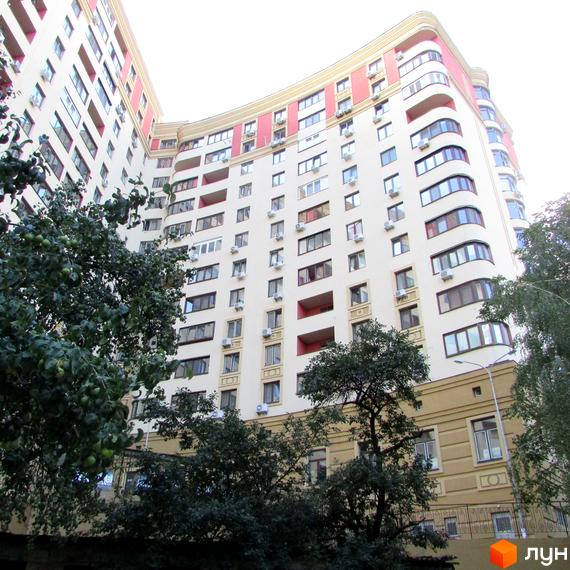 Житловий комплекс Златоустівський – багатоповерховий будинок з вигнутим фасадом, балконами та кондиціонерами. Навколо будівлі зелені дерева та зелень.