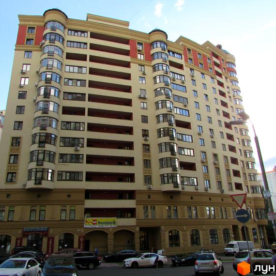 Зовнішній вигляд житлового комплексу Златоустівський з безліччю балконів та вікон. Навколо будинку розташовані автомобілі та дерева.