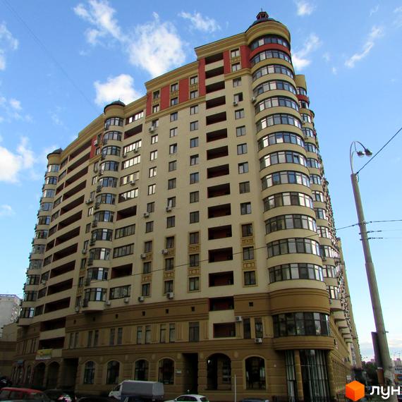 Житловий комплекс Златоустівський – висотна будівля з багатоповерховими квартирами, вигнутим фасадом та балконами. Навколо будинку розташовані припарковані автомобілі та міська інфраструктура.