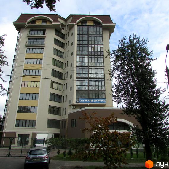 Житловий комплекс Нагірний з великими вікнами та прибудинковою територією, озелененою деревами та кущами.