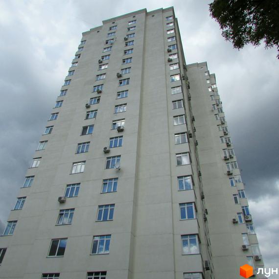 Житловий комплекс Затишний дім - висотна багатоповерхівка з численними вікнами та кондиціонерами на фасаді. Будинок має світле оздоблення та розташований на фоні хмарного неба.