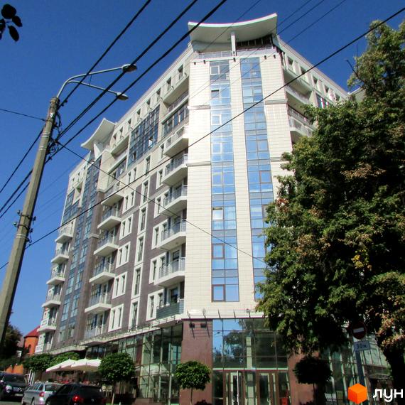 Житловий комплекс Zverinetskiy з сучасним фасадом та великими вікнами. Прибудинкова територія озеленена деревами та має зону для відпочинку.