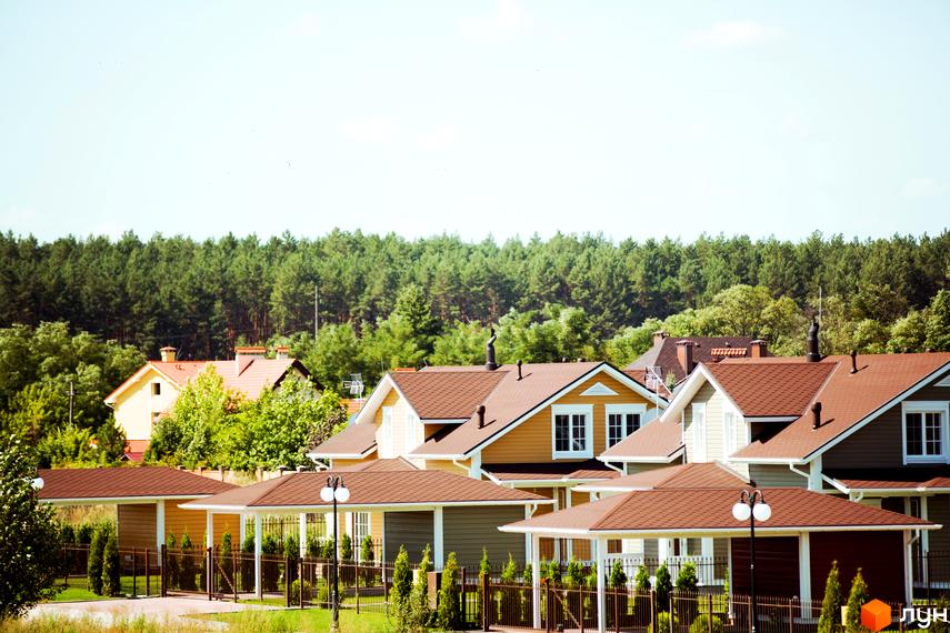 Котеджне містечко Бобриця-Парк. Одноповерхові будинки з коричневими дахами та білими вікнами. На території є зелені насадження та огорожа.