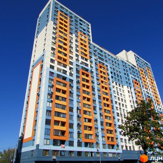Житловий комплекс Богатирський - висотна новобудова з яскравим фасадом у блакитних та помаранчевих тонах. Будинок має багато вікон та балконів, на тлі чистого синього неба.