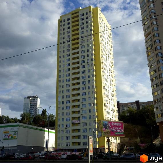 Житловий комплекс на Саперно-Слобідській, 24 – висотна жовто-біла новобудова з численними балконами. Навколо будівлі розташована парковка та зелені насадження.