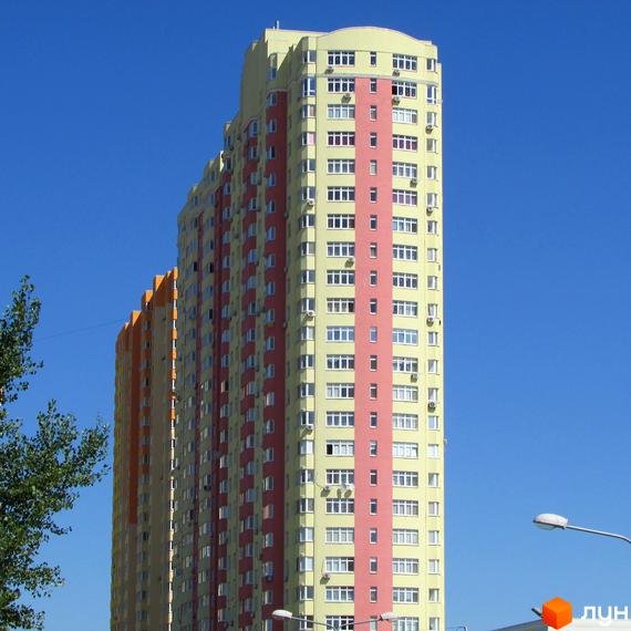Житловий комплекс Яскравий - висотна новобудова з жовто-рожевим фасадом. Будинок має багато вікон та кондиціонерів, розташований на фоні блакитного неба.