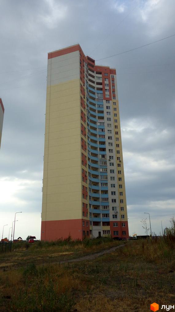 Багатоповерховий житловий комплекс на вулиці Милославській, 2, 2б, 2в. Будинок має світло-жовту, білу та помаранчеву облицювання. Навколо будинку зелена територія з деревами та травою.