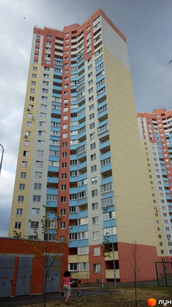 Багатоповерховий житловий комплекс на вул. Милославська, 2, 2б, 2в. Будинок має секції з різним кольоровим оздобленням фасадів: білий, жовтий, блакитний та рожевий. На прибудинковій території видно дерева та дитячий майданчик.