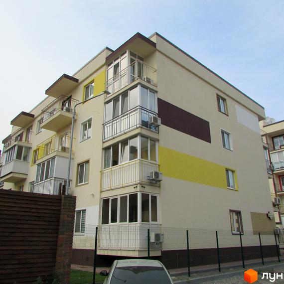 Фасад житлового комплексу Власна Квартира з балконами та кондиціонерами. Прибудинкова територія з парканом та деревами.