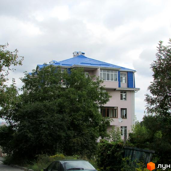 Новобудова з блакитним дахом на пров. Іллі Рєпіна (Шишкінський). Будинок оточений зеленню, видно дерева та частину автомобіля.