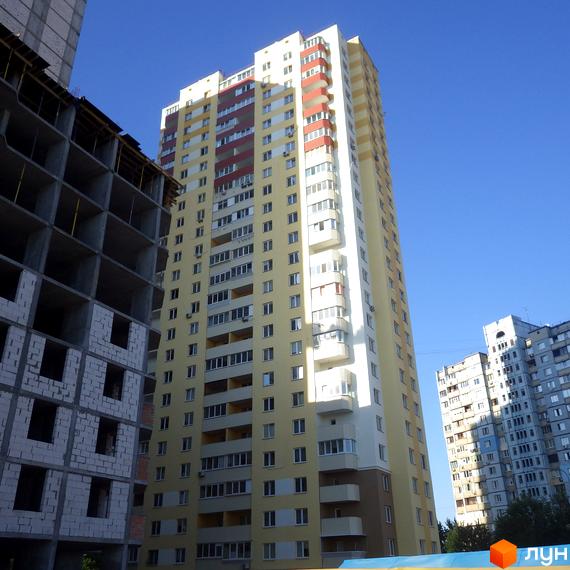 Новобудова на вулиці Хорольська, 1а. Висотна жовта будівля з червоними та білими елементами фасаду на фоні блакитного неба. Поруч видно будівельний майданчик.