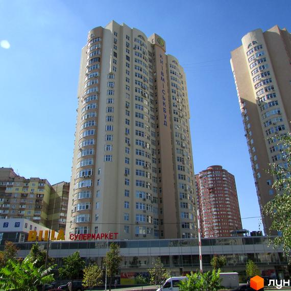 Високоповерховий житловий комплекс на вулиці Драгоманова, Київ. Будинок має світло-бежевий фасад та багато вікон. Біля комплексу розташований супермаркет.