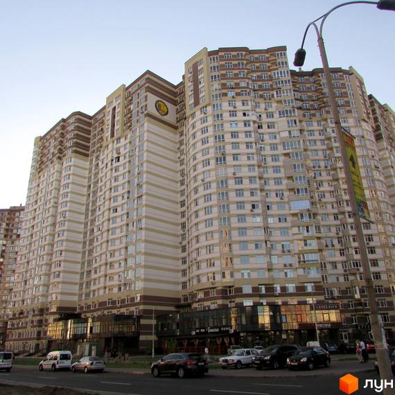 Житловий комплекс Діамант на Ахматової, 22. Багатоповерхова будівля з бежево-коричневим смугастим фасадом, вікнами та комерційними приміщеннями, поруч дорога з авто.