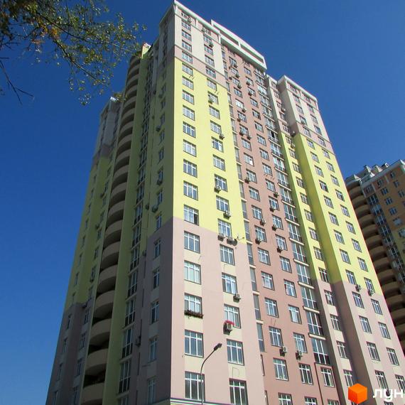 Фото багатоповерхового будинку на вул. Гната Хоткевича, 8. Житловий комплекс з великою кількістю вікон та балконів на фоні блакитного неба.