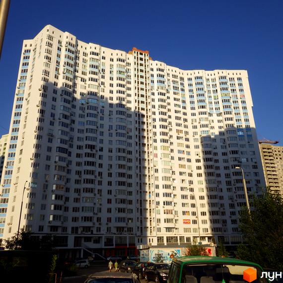 Зображення багатоповерхового будинку на вулиці Єлизавети Чавдар, 13. Білий фасад з великою кількістю вікон, видно частину прибудинкової території з автомобілями.