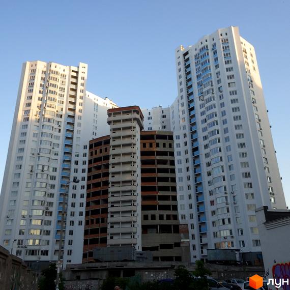 Зображення житлового комплексу по вул. Єлизавети Чавдар, 13. Висотні будинки з великою кількістю вікон, поряд недобудована будівля.