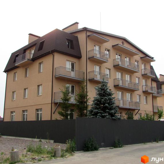 Зображення чотириповерхового будинку в Житловому комплексі Цитадель „Теремки“ з балконами та мансардним дахом. Перед будинком зелені насадження та сірий паркан.