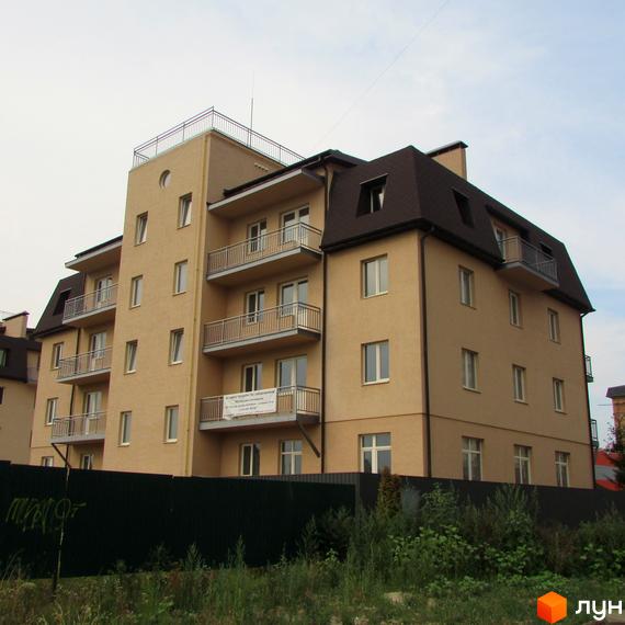 Фото фасаду чотириповерхового будинку в Житловому комплексі Цитадель „Теремки“ з балконами. Навколо будинку зелені насадження та невисокий паркан.