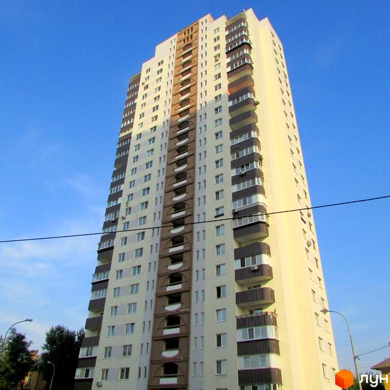 Висотна будівля житлового комплексу з балконами та вікнами. На передньому плані видно лінію електропередач та зелені насадження.
