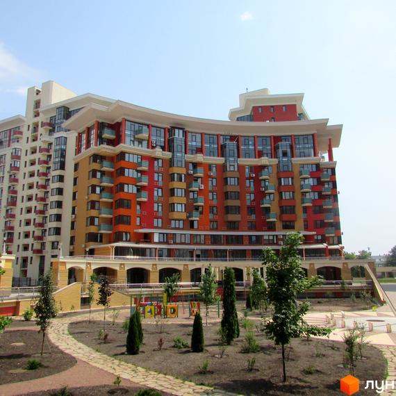 Житловий комплекс Сонячна брама з кольоровим фасадом та великими вікнами. Прибудинкова територія з дитячим майданчиком та зеленими насадженнями.