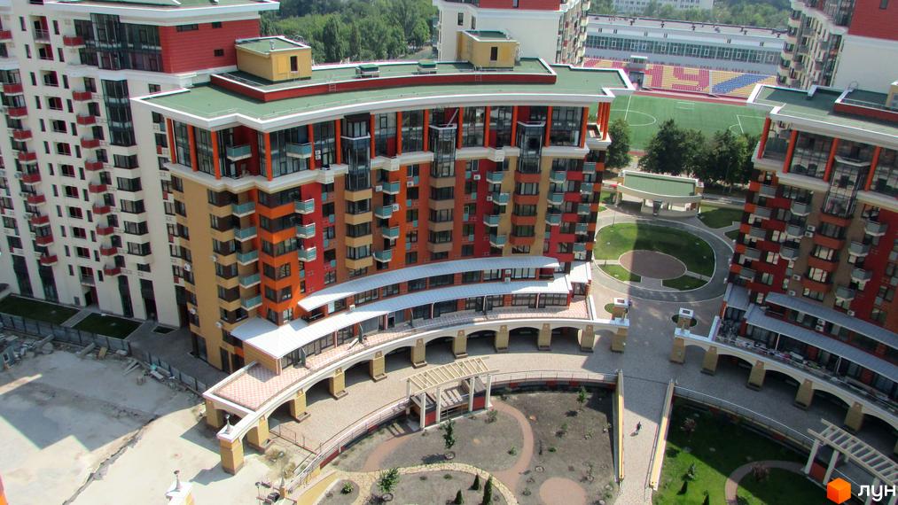 Багатоповерхові будинки Житлового комплексу Сонячна брама з різнокольоровими фасадами та балконами. Видно внутрішній двір з доріжками, зеленню та спортивний стадіон поруч.