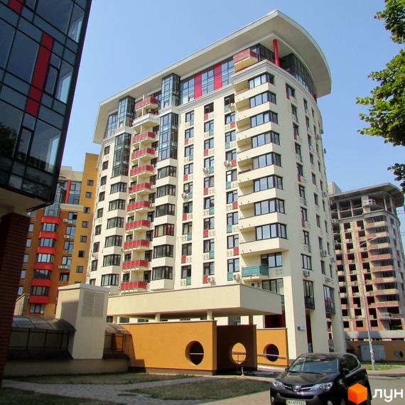 Житловий комплекс Сонячна брама: світлий багатоповерховий будинок з червоними балконами та вигнутим дахом. Прибудинкова територія з газоном.