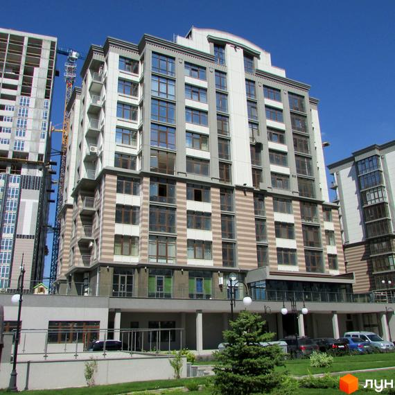 Багатоповерховий будинок Житлового комплексу Новопечерські Липки з фасадом світлих відтінків та великими вікнами. Навколо будинку зелений газон, дерева та парковка для автомобілів.