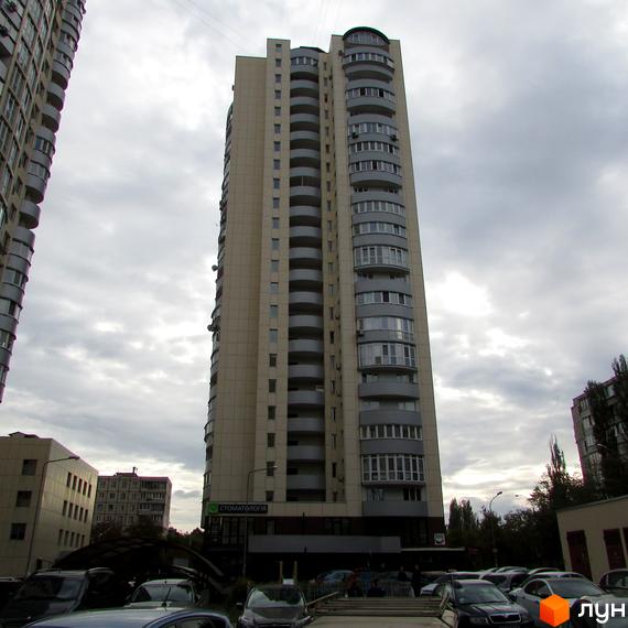 Житловий комплекс Парковий: високий будинок світлого кольору з округлими балконами. Перед комплексом видно парковку з автомобілями та комерційні приміщення.