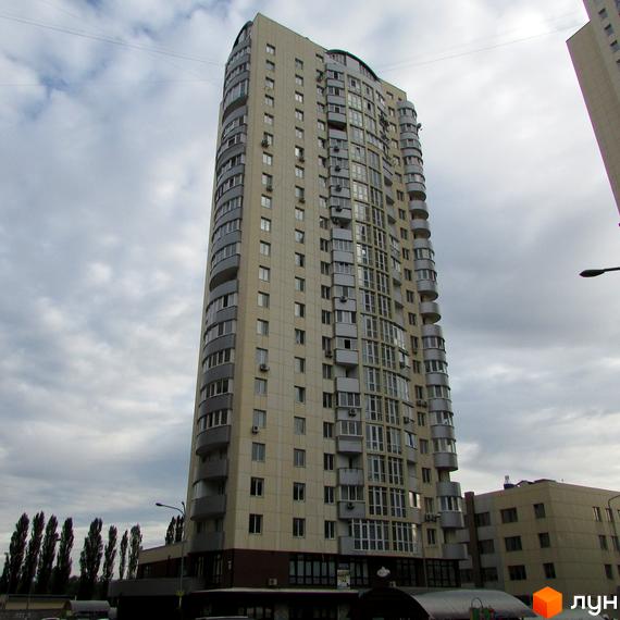 Висотна житлова будівля світлого кольору з численними вікнами та балконами. Житловий комплекс Парковий на тлі хмарного неба, поруч дерева.