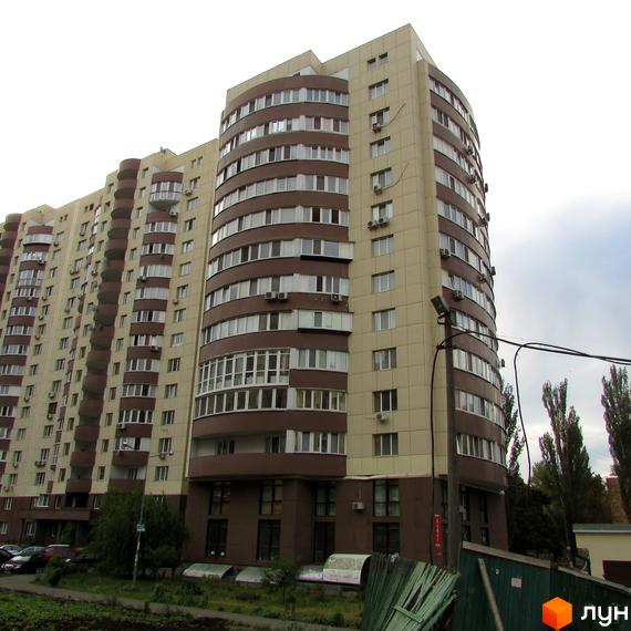 Фасад житлового комплексу Парковий бежево-коричневого кольору з округлими секціями та балконами. Перед будинком видно припарковані автомобілі та зелені насадження.