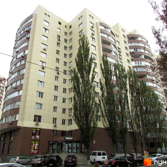 Багатоповерховий житловий комплекс Парковий з бежево-коричневим фасадом та балконами. Перед будинком розташовані дерева та припарковані автомобілі.