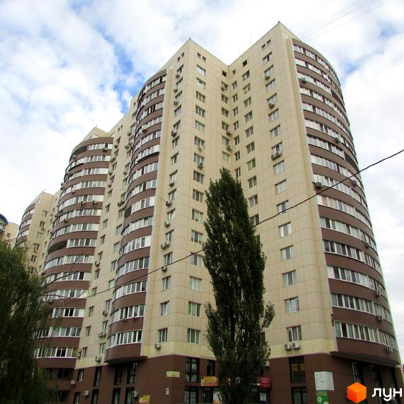 Фасад житлового комплексу Парковий виконаний у бежевих та коричневих тонах, з округлими та прямими секціями. Перед будинком розташовані високі дерева.