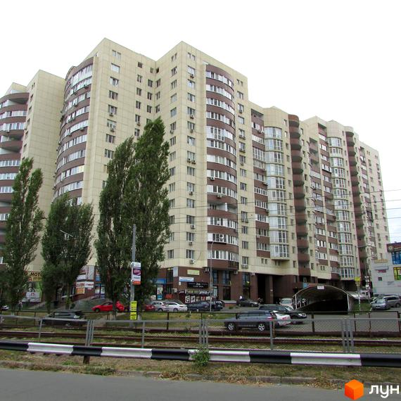 Житловий комплекс Парковий з фасадом з панорамними вікнами та прибудинковою територією, де розташовані автомобілі та дерева.